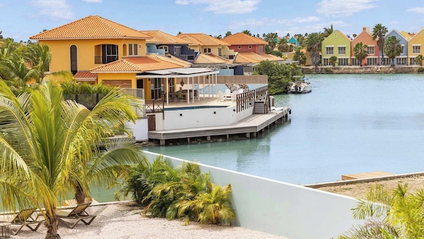 A waterfront property with a pool, lounge chairs, and a dock with a boat. - Kas Blou Blou with refreshing communal pool (Kralendijk)