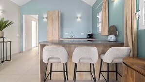 A modern kitchen with a bar area, featuring three bar stools, a wooden countertop, and a light blue wall. - Kas Blou Blou with refreshing communal pool (Kralendijk)