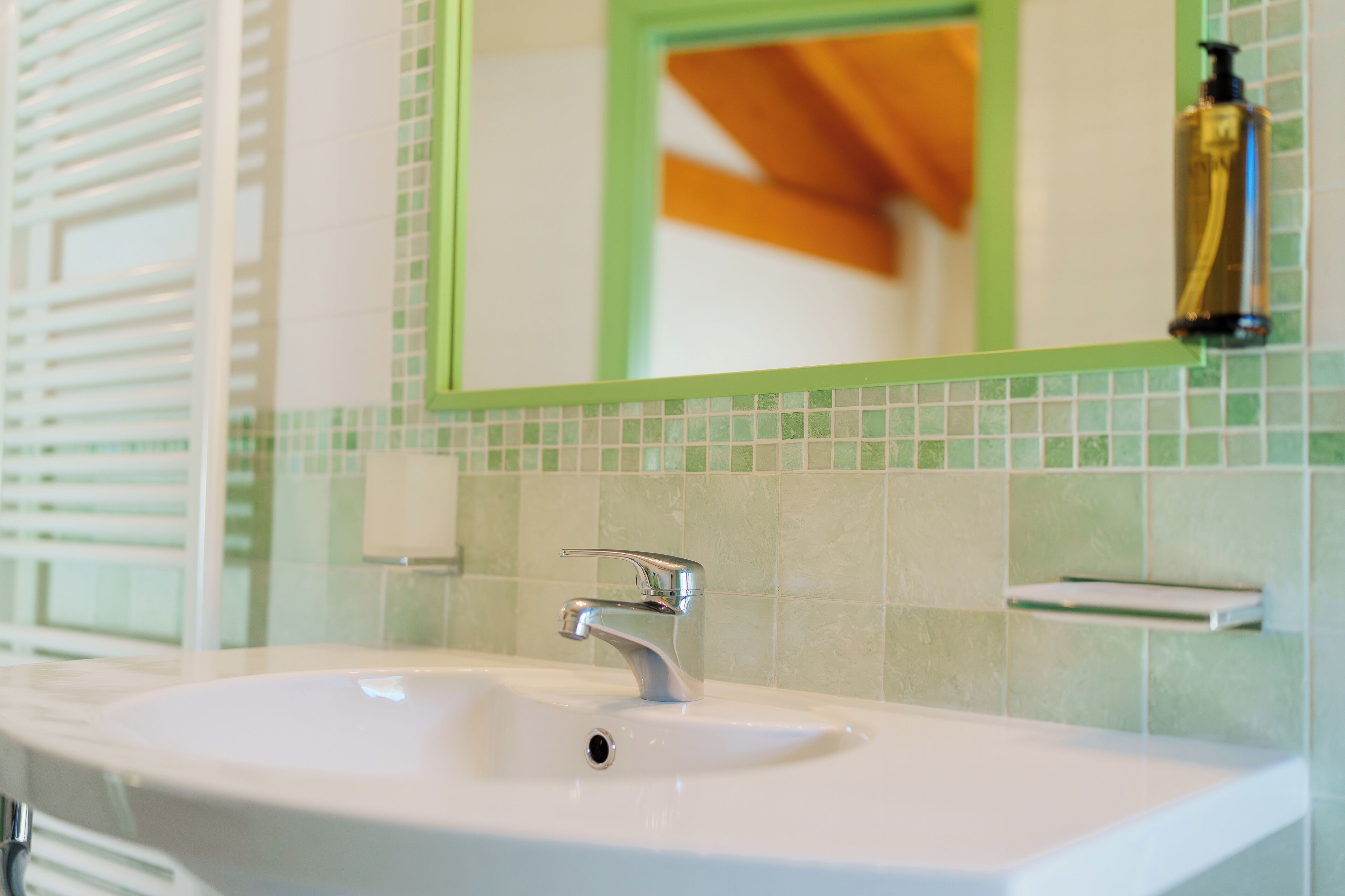 Um banheiro com pia branca, paredes revestidas de azulejos verdes e espelho com moldura verde.