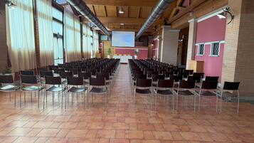 A conference room with rows of chairs, a stage, and a projector screen.