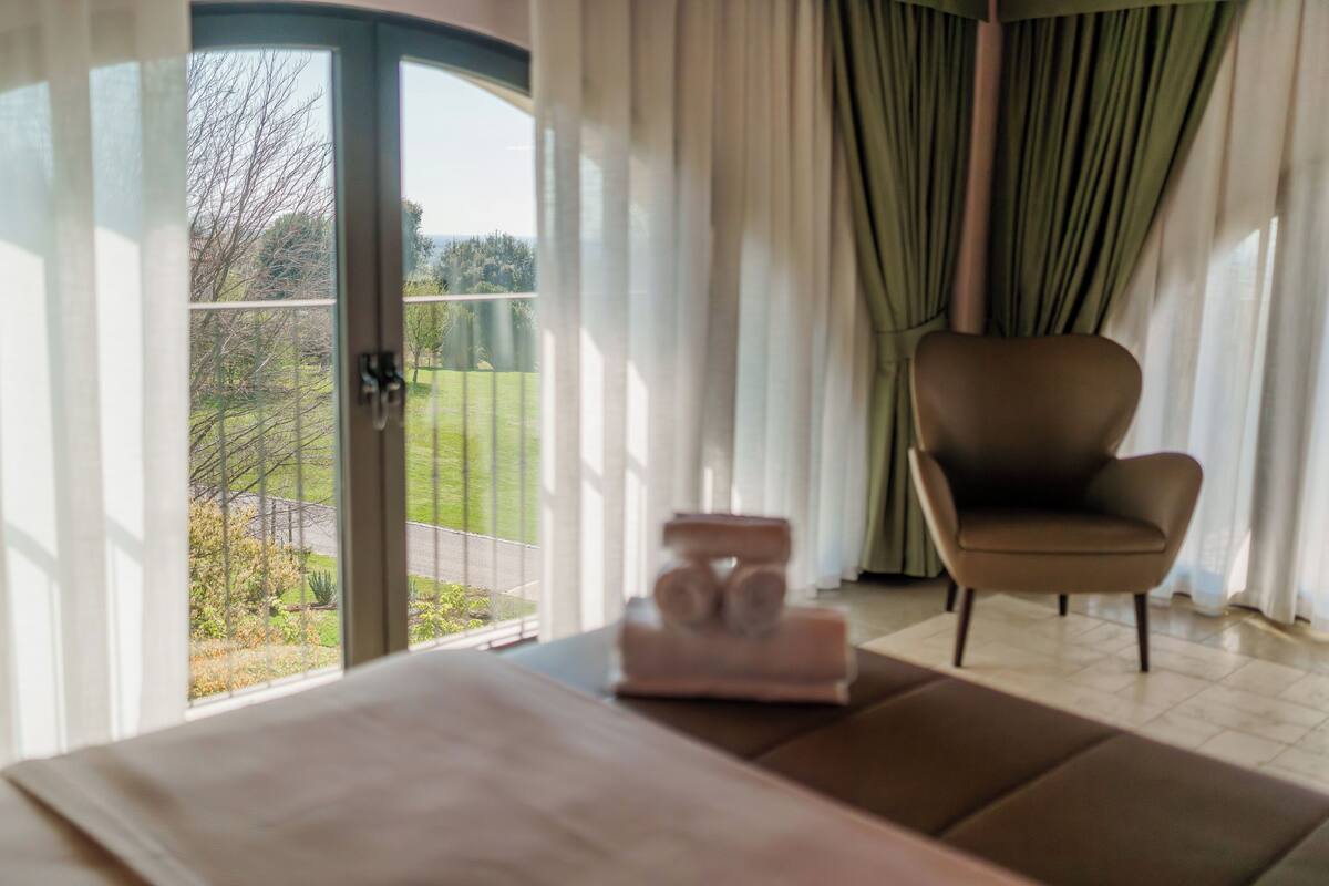 A room with a view of a garden through a glass door, a brown chair, and a small table with a decorative item.