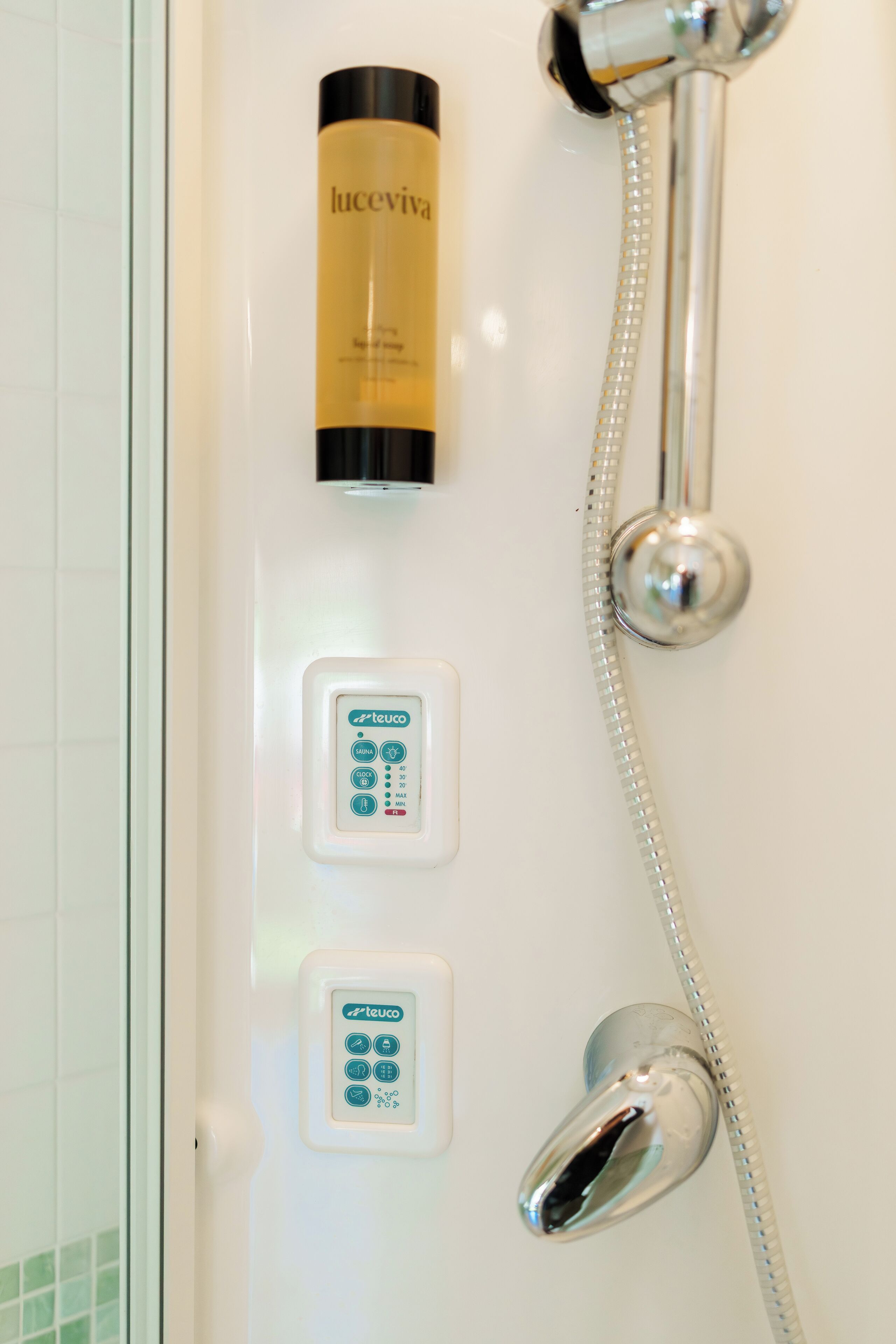 A bathroom with a shower, a control panel, and a bottle of lotion.
