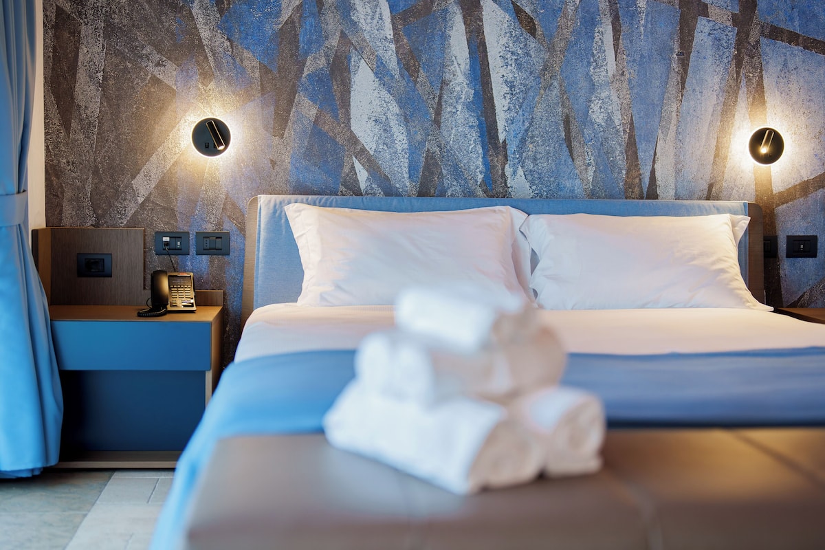 A neatly made bed with white linens and a folded towel on the bedside table.