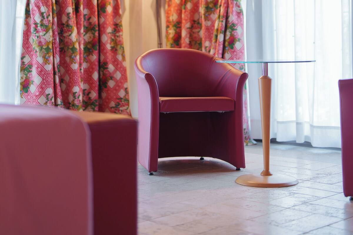 A room with a wooden ceiling, floral curtains, a red chair, and a floor lamp.