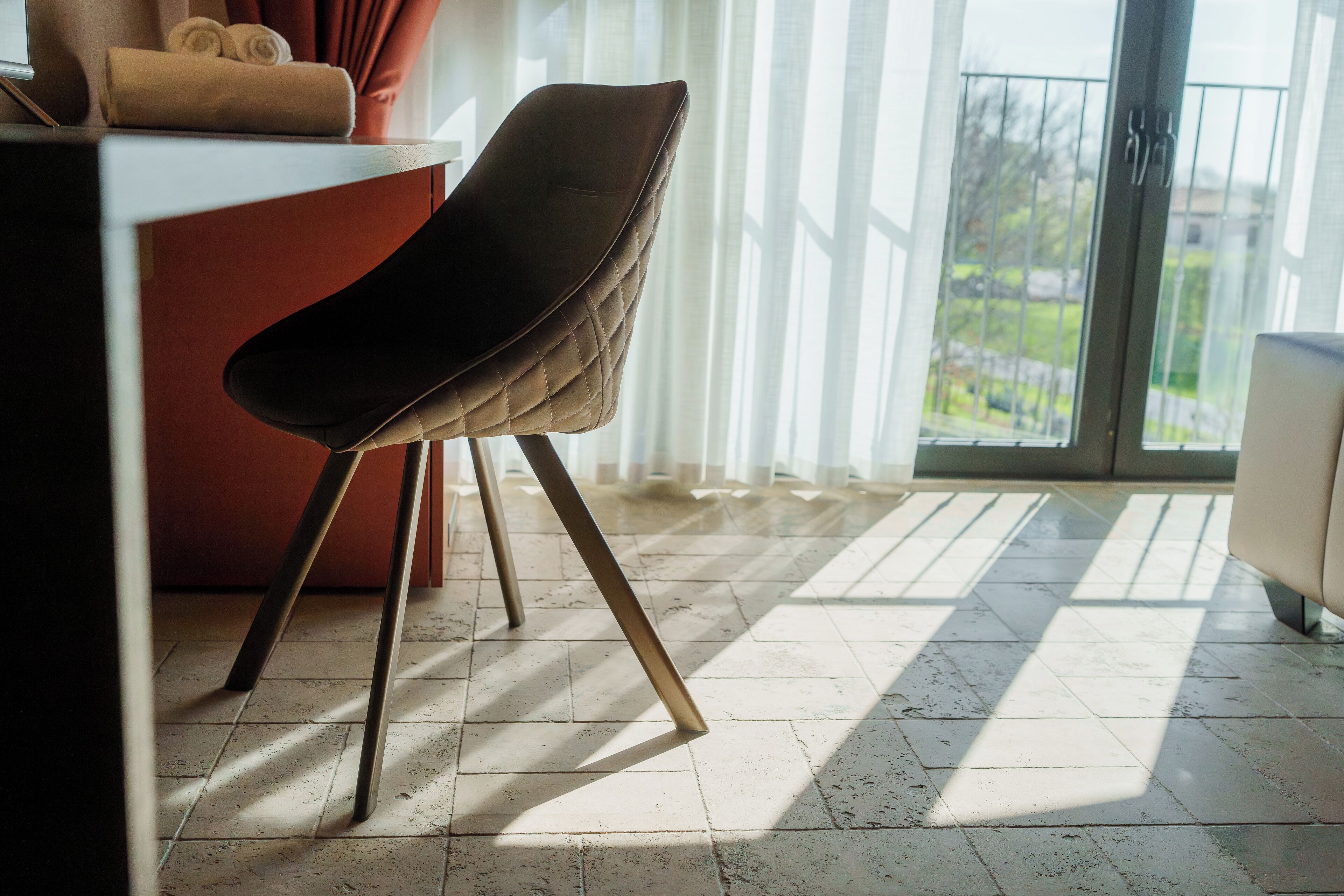 Ein moderner Essbereich mit einem dunkel gepolsterten Stuhl, einem roten Tisch und Blick auf einen Garten durch große Fenster.