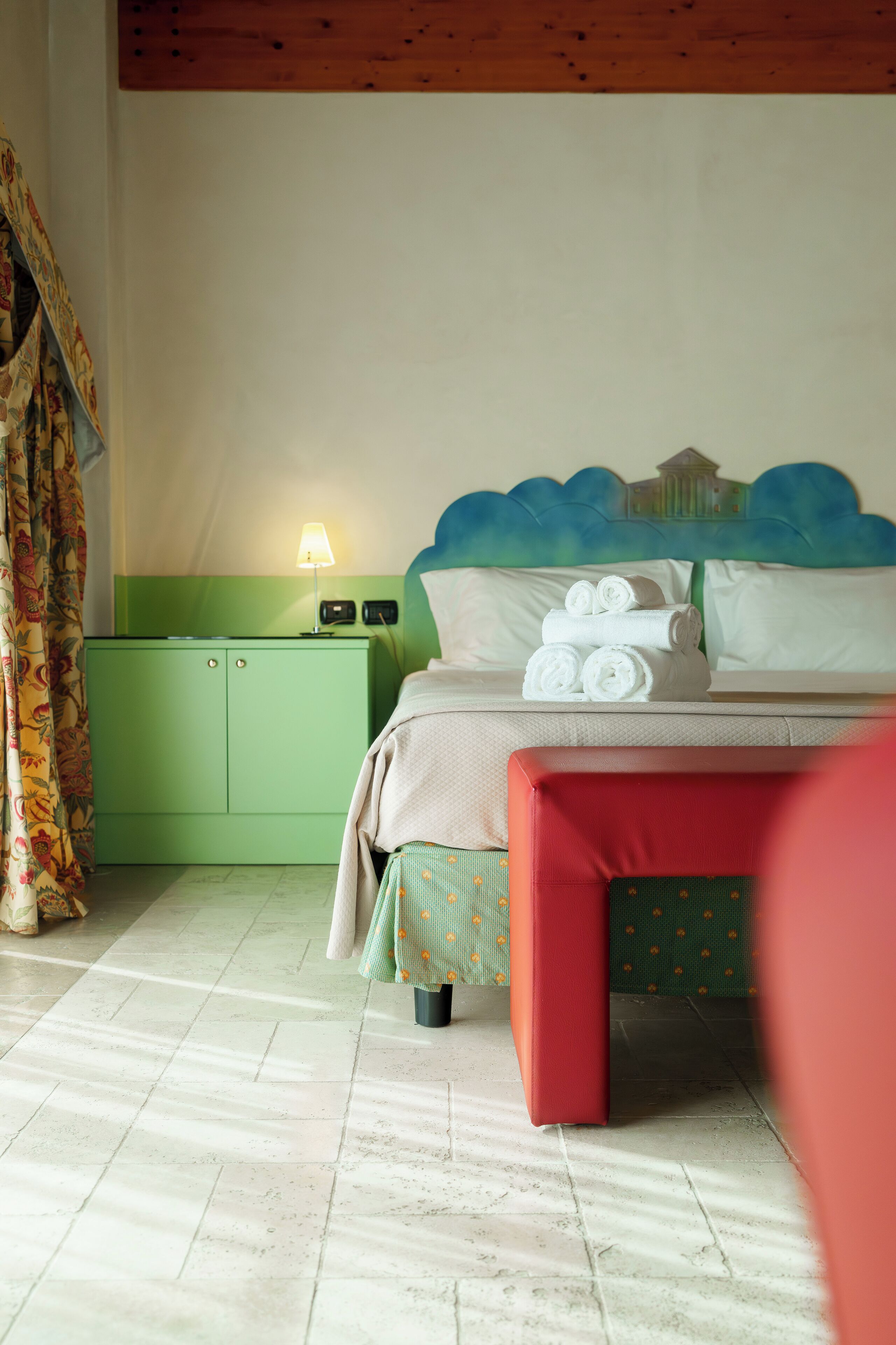 Een hotelkamer met een bed, een nachtkastje in het groen met een lamp, en een rode bank.