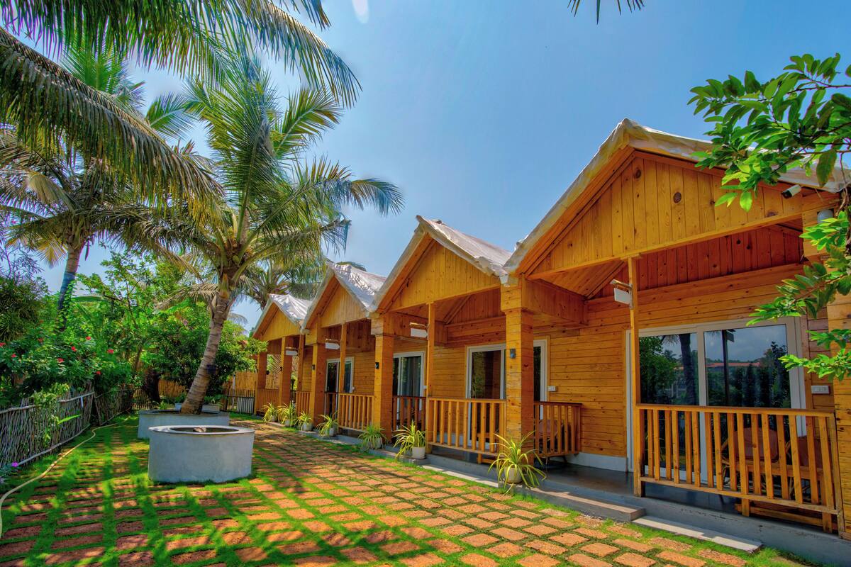 A row of wooden cabins with a paved walkway and palm trees.