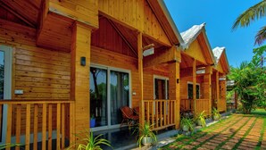 A wooden cabin with a porch, sliding glass doors, and potted plants. - The Lazy Cabanas (Candolim)