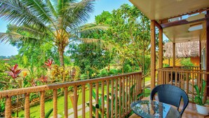A balcony with a glass table and wicker chairs, surrounded by lush tropical plants and a wooden railing. - The Lazy Cabanas (Candolim)