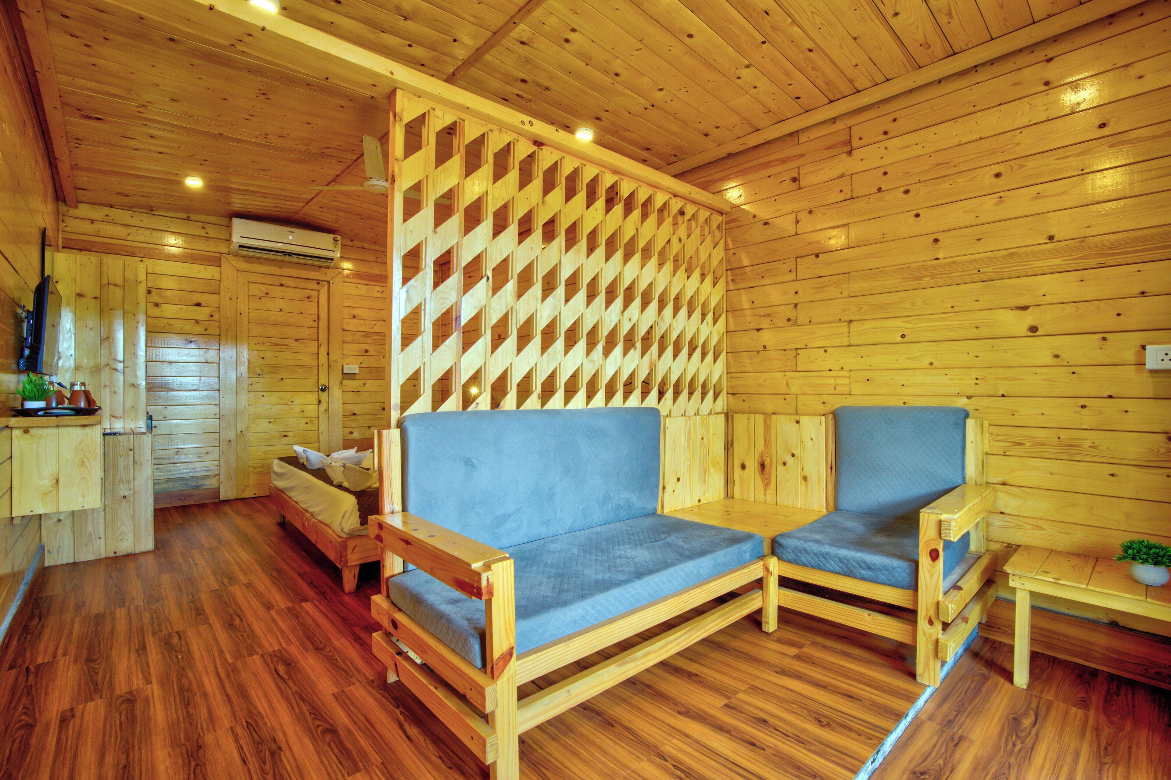 Interior de una cabaña de madera con sofá, dos sillones, una mesita con una planta y un mamparo de madera.