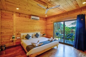Quarto de cabana de madeira com cama, ventilador de teto e vista para o exterior.