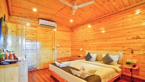 A wooden cabin bedroom with a bed, bedside table, and a ceiling fan. - The Lazy Cabanas (Candolim)