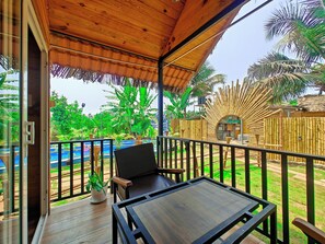 Um deck de madeira com mesa e cadeiras, cercado por uma vedação de bambu e plantas tropicais.