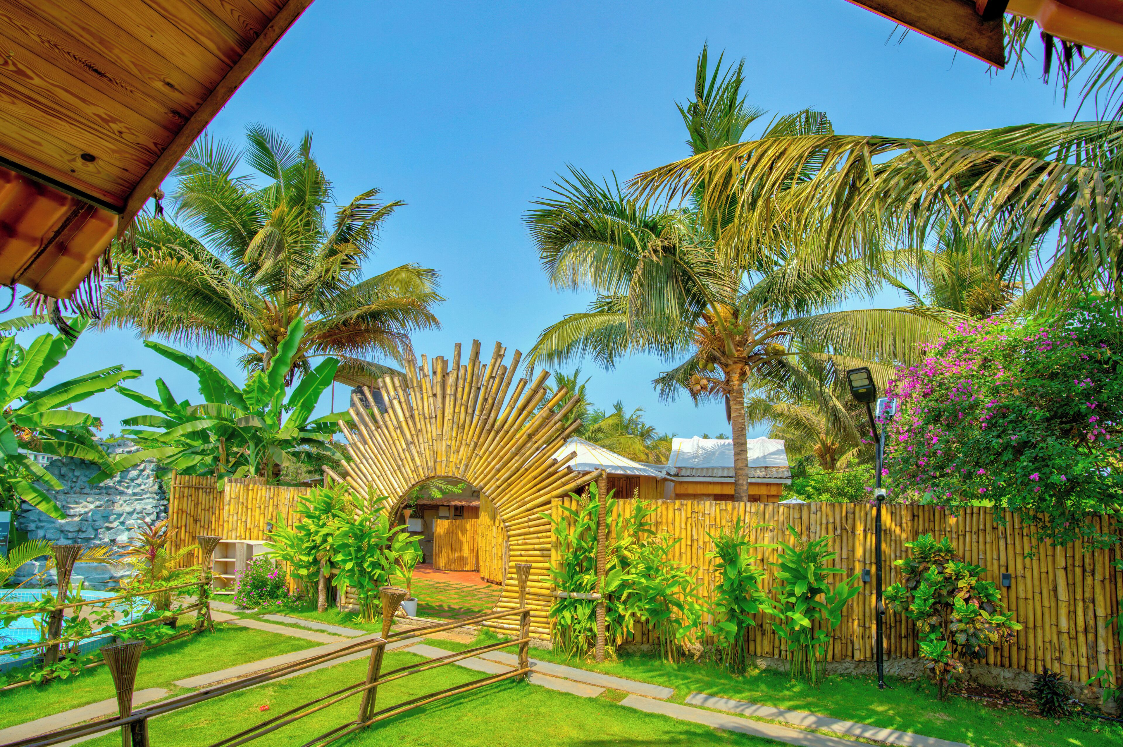 Un resort tropical con un arco de bambú, palmeras y una piscina.