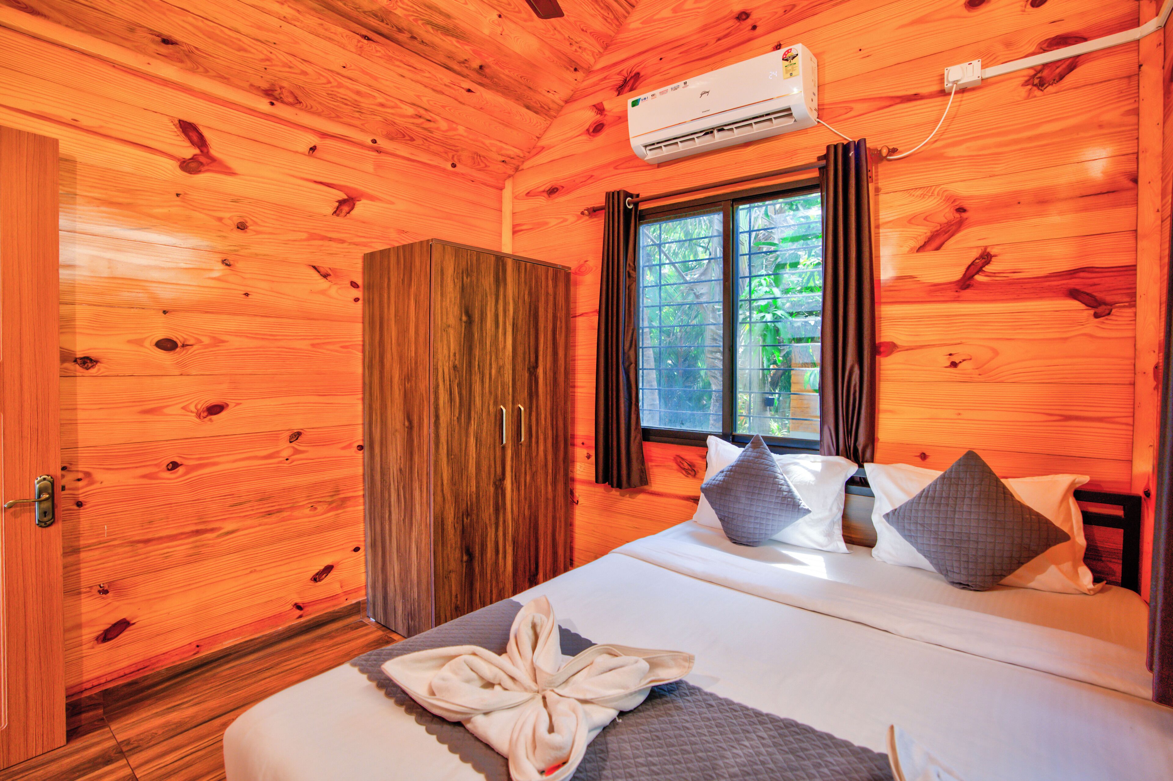 A wooden cabin bedroom with a bed, pillows, a robe, and a window with curtains.