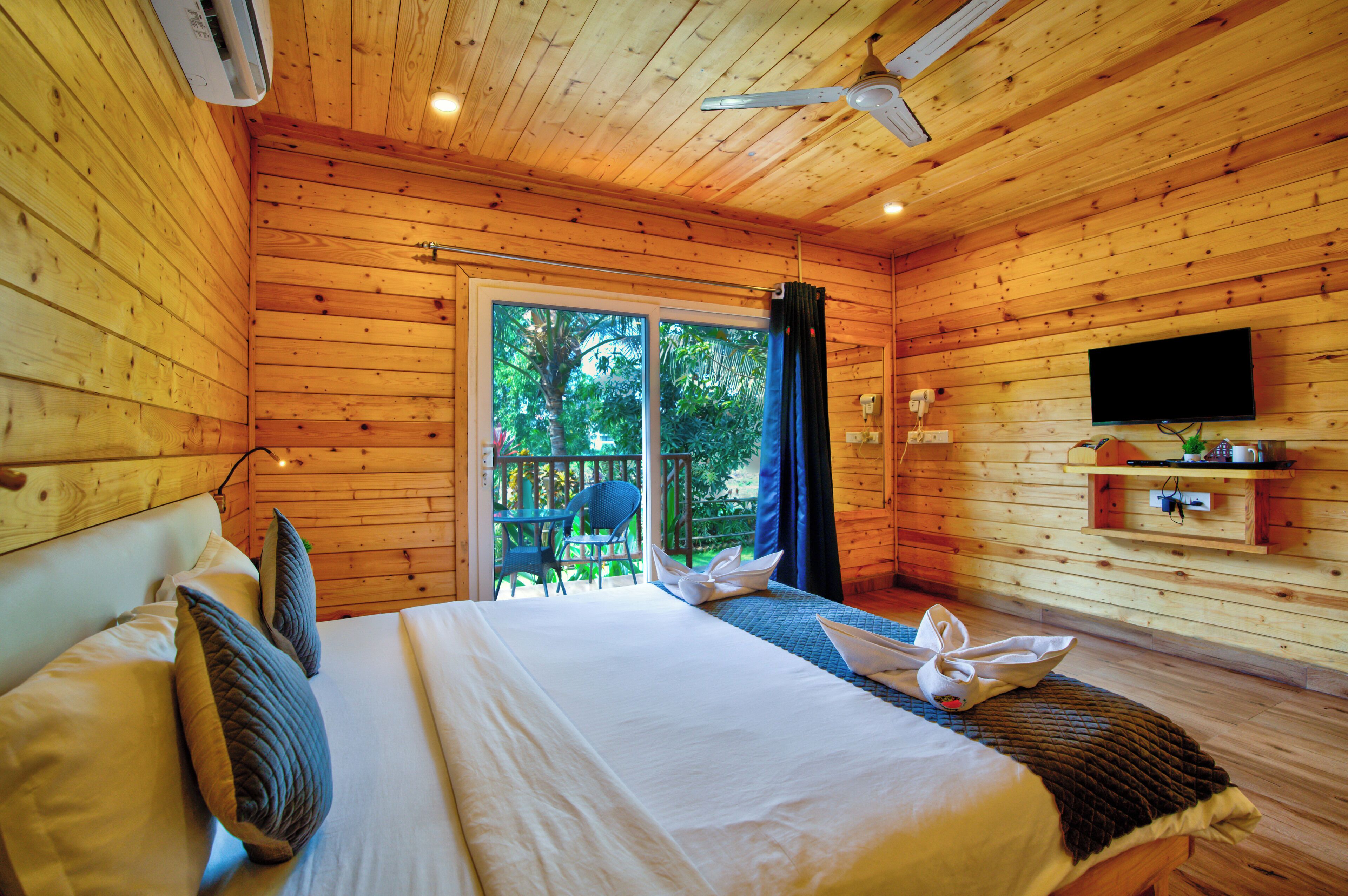Une chambre de style cabane en bois, équipée d’un lit, d’un ventilateur de plafond, d’une télévision et d’une porte-fenêtre coulissante donnant sur l’extérieur.
