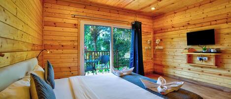 Une chambre de style cabane en bois, équipée d’un lit, d’un ventilateur de plafond, d’une télévision et d’une porte-fenêtre coulissante donnant sur l’extérieur.