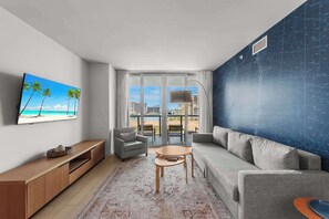 Een moderne woonkamer met een groot raam, een flatscreen televisie, een bank, een fauteuil en een kleine tafel.