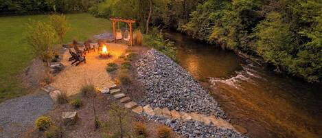 A riverside patio with a fire pit, seating, and a pergola.