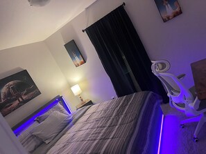 Ein Hotelzimmer mit einem Bett, einem Schreibtisch, einem Sessel, einem Nachttisch, einer Lampe und einem Wandbild.