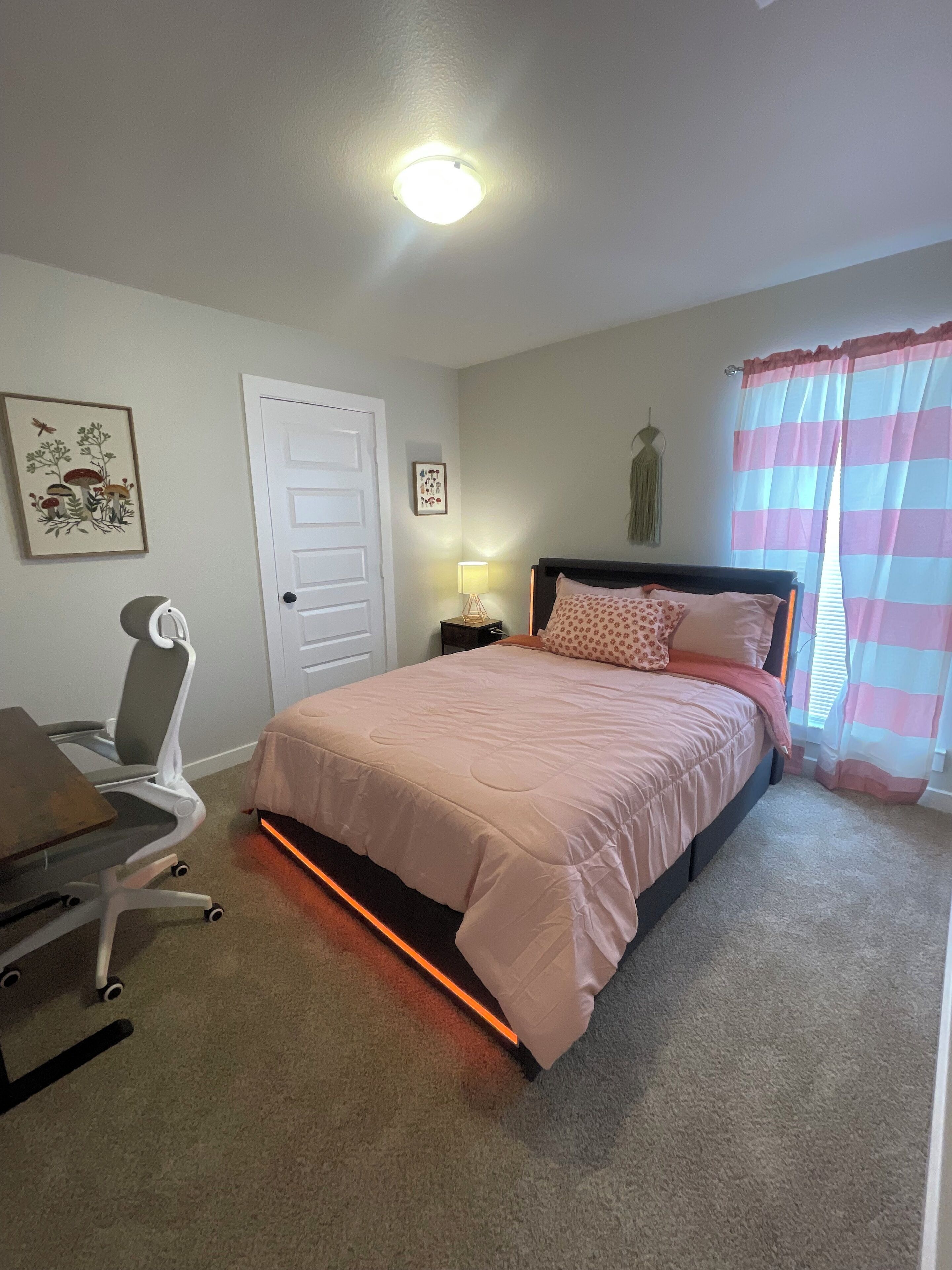 Un dormitorio con cama, escritorio, silla, puerta y ventana con cortinas.