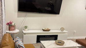 Una sala de estar moderna con un sofá de cuero, un televisor de pantalla plana montado en la pared, una mesita auxiliar con objetos decorativos y una mesa de centro con un cuenco.