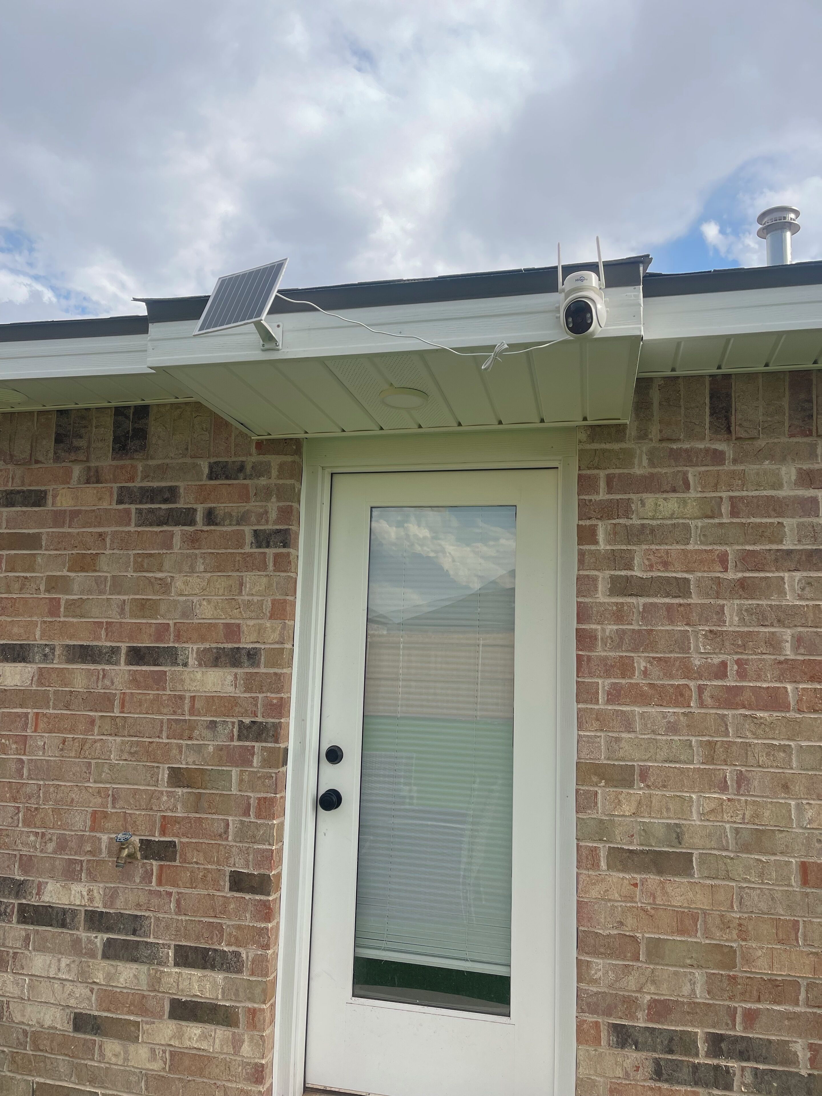 A brick building with a white door, a window with blinds, and a solar panel on the roof.