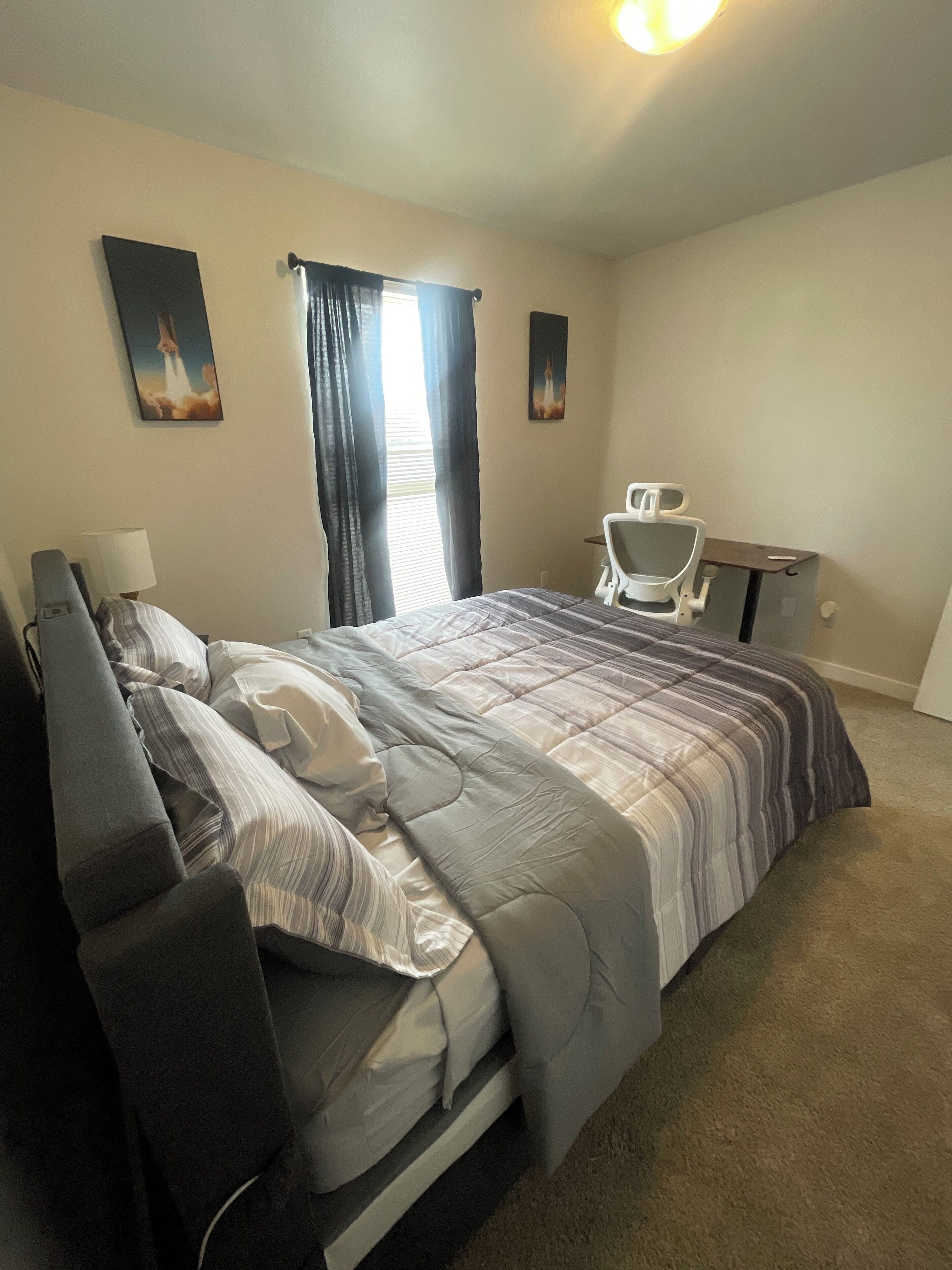 Une chambre d’hôtel avec un lit, un bureau, une chaise et deux tableaux accrochés au mur.