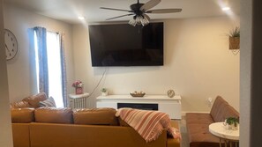 Ein Wohnzimmer mit einer Couch, einem Couchtisch, einem an der Wand befestigten Fernseher und einem Deckenventilator.