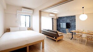 Een moderne hotelkamer met een groot bed, een slaapbank, een zithoek met een tafel en stoelen, en een aan de muur bevestigde televisie.