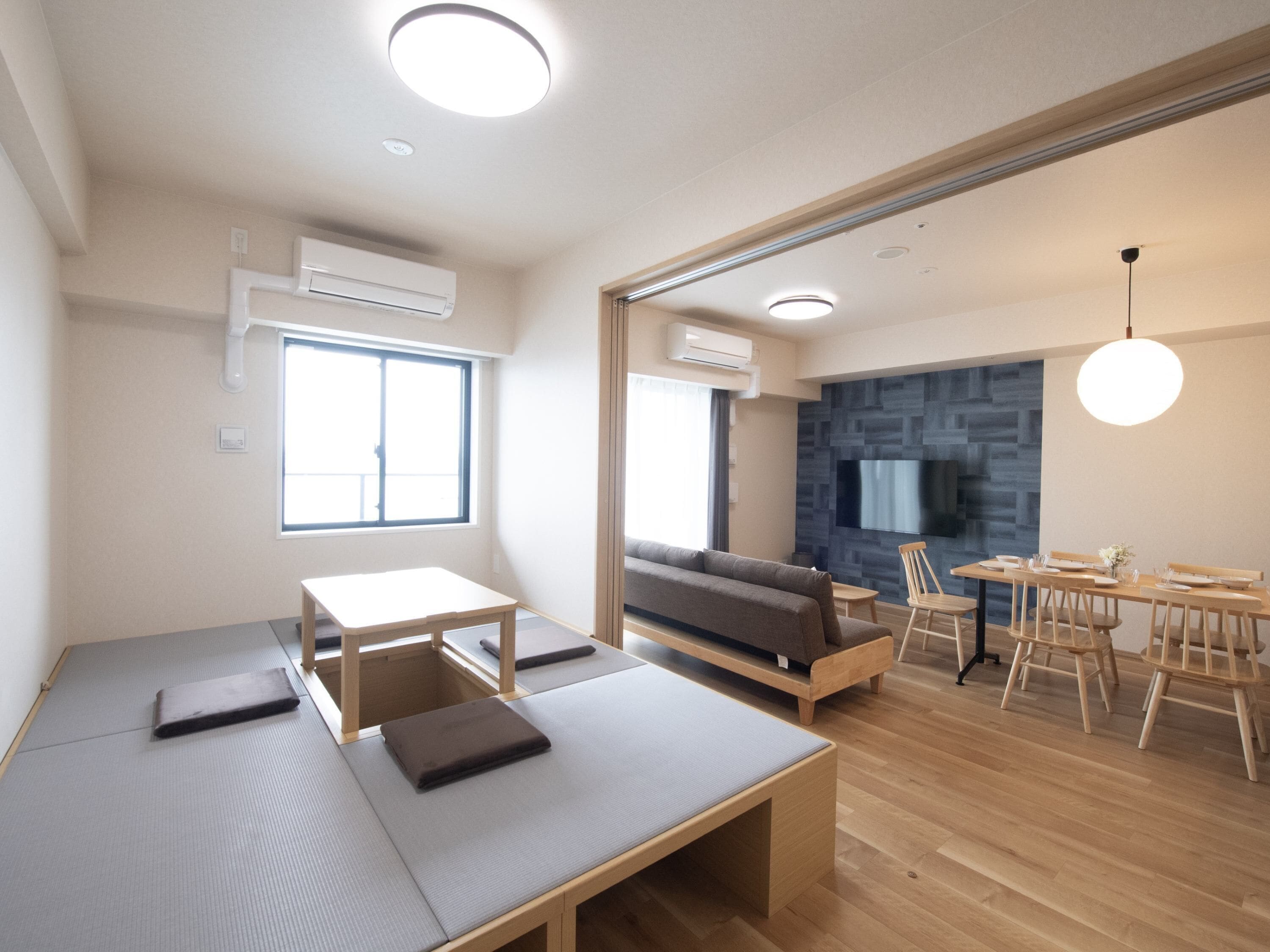 Una sala de estar moderna con un sofá, una mesa de comedor con sillas, una pequeña cocina y un ventanal grande.