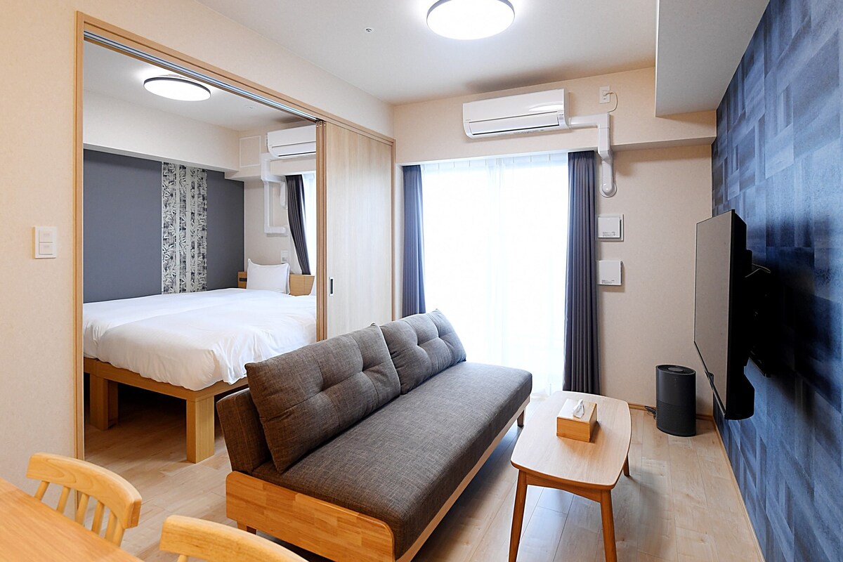 Habitació d'hotel moderna amb sofà, taula petita, llit i televisió.