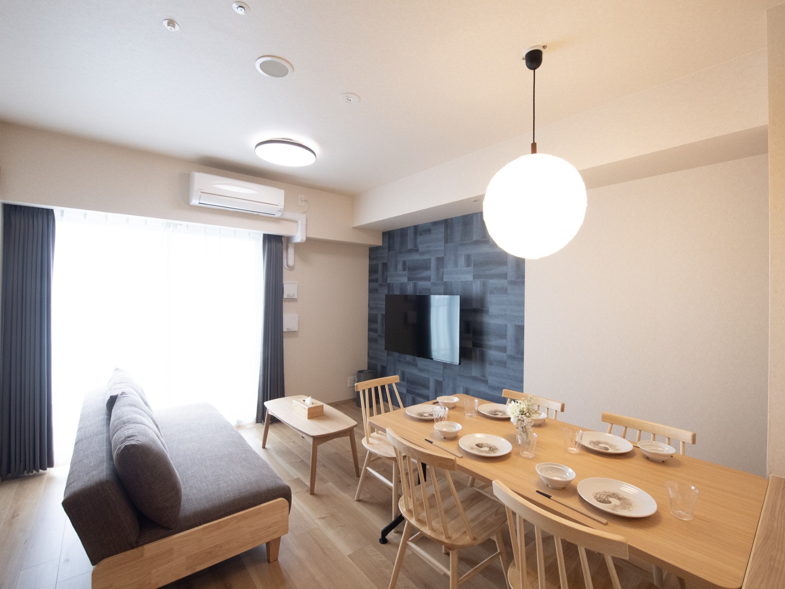 A modern dining area with a wooden table set for four, a sofa, and a TV mounted on the wall.