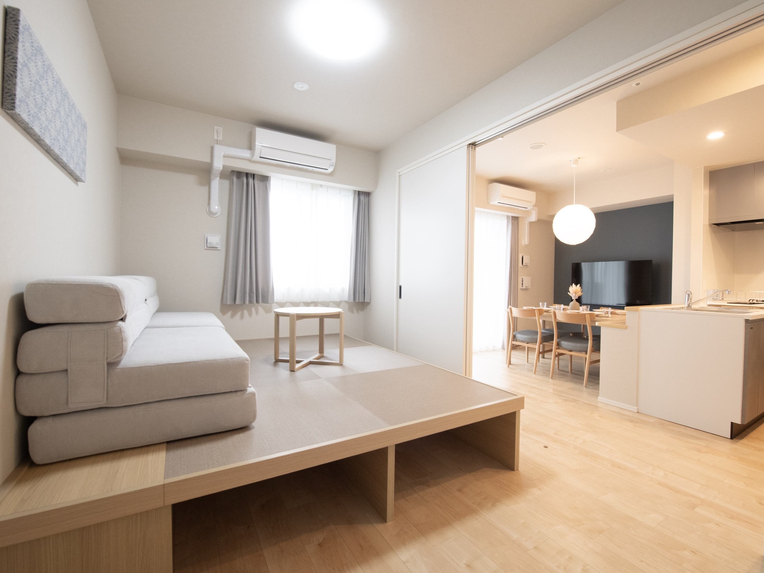 A modern, minimalist living room with a sofa, a small table, and a kitchen area visible through an open door.