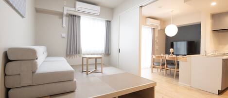 A modern, minimalist living room with a sofa, a small table, and a kitchen area visible through an open door.