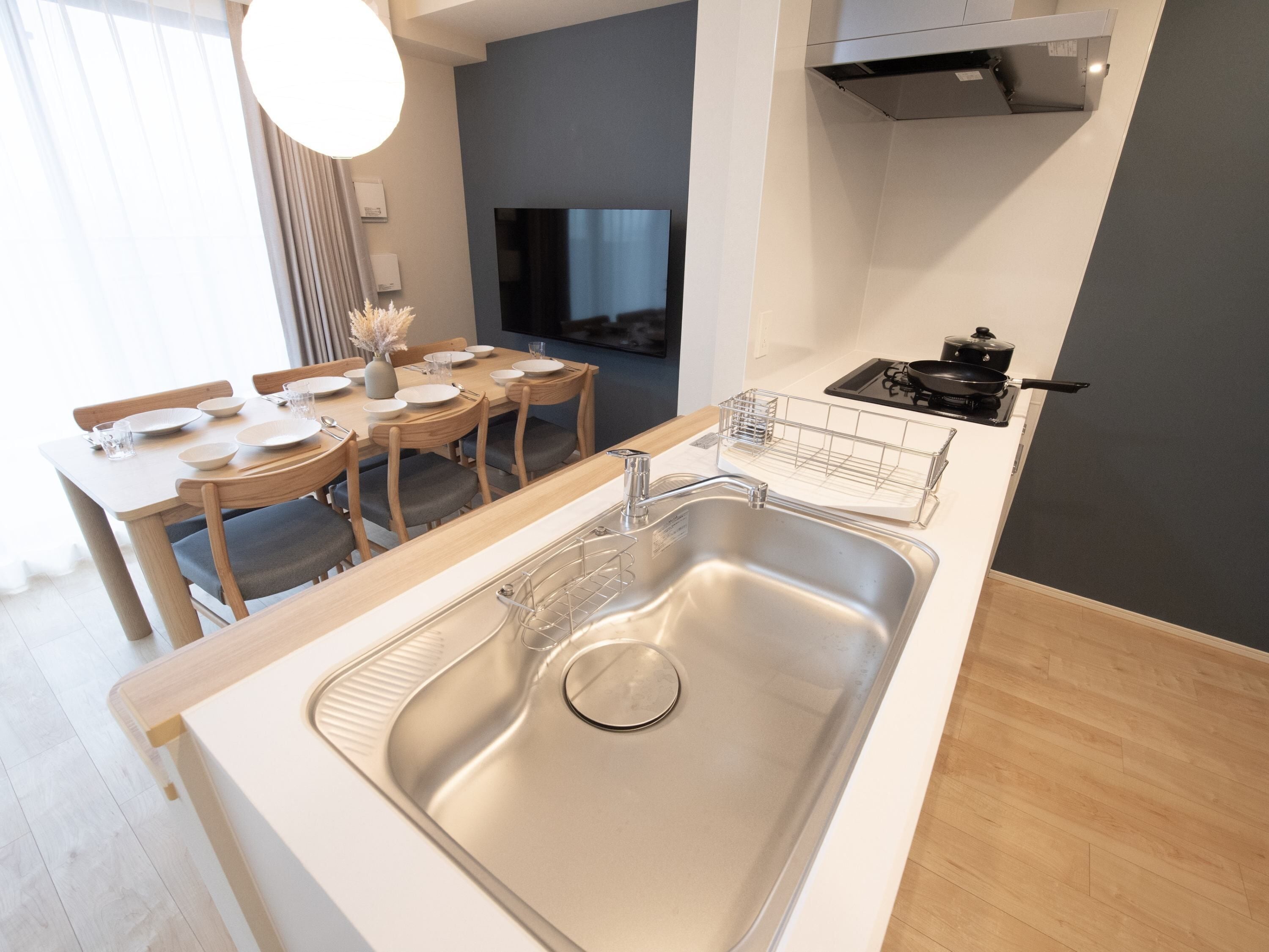 A modern kitchen with a stainless steel sink, wooden dining table, and chairs.