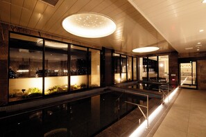 A modern indoor pool area with glass walls, a central water feature, and a reception desk. - THE RISE OSAKA UNIVERSAL BAYSIDE (Osaka)