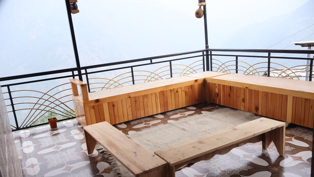 Un banc et une table en bois sont placés sur un sol à motifs, et offrent une vue sur la mer à travers une rambarde en métal.