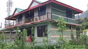 Une maison à deux étages avec un balcon, un toit rouge et une façade verte.