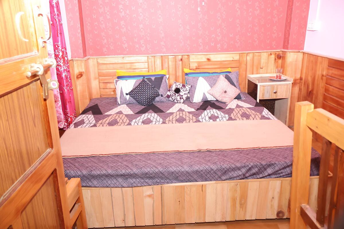 A wooden-paneled room with a bed, a nightstand, and a window with curtains.