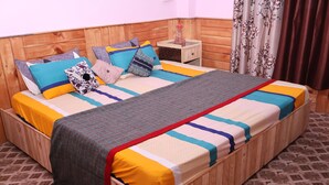 Un lit en bois avec une couvre-lit et des oreillers aux couleurs vives, une petite table de chevet avec une bouteille, et des rideaux à motifs.