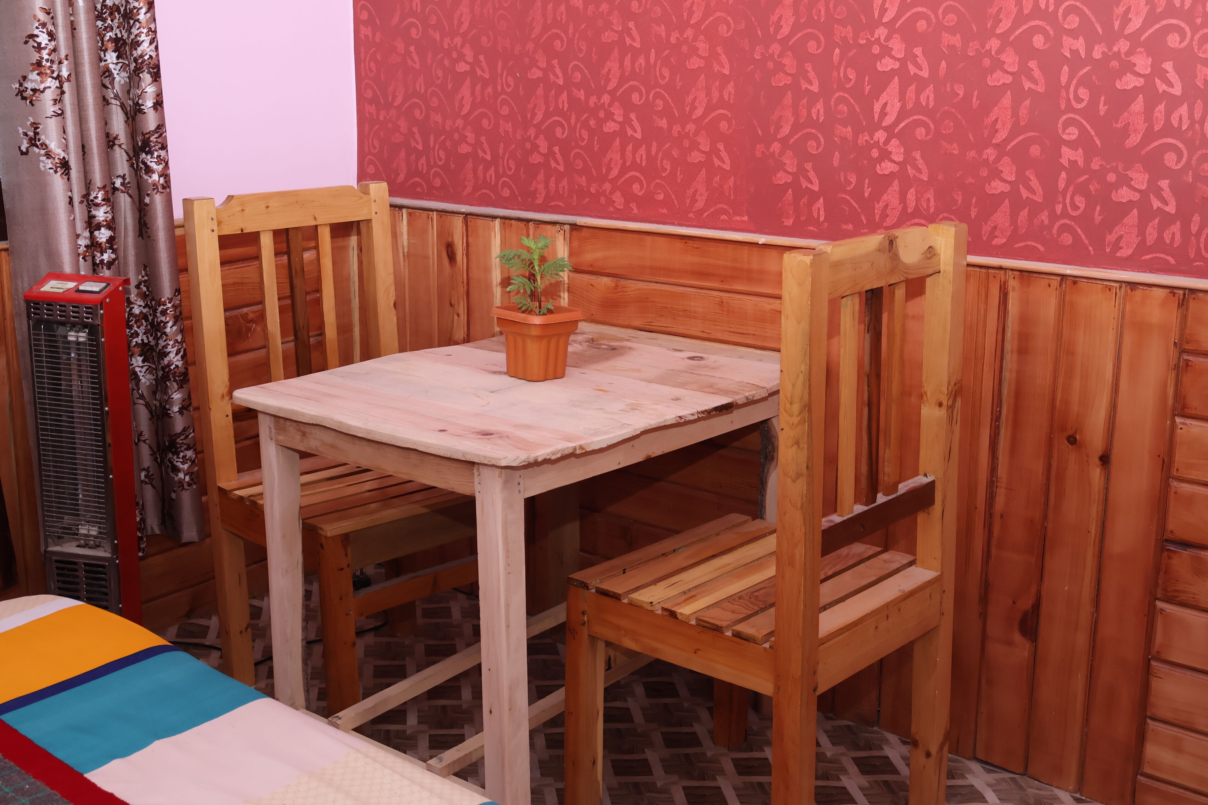 Une table en bois, deux chaises, une plante en pot et un mur décoré d’un motif rouge.