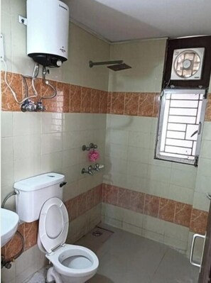 Une salle de bain équipée de toilettes, d’un lavabo, d’une douche et d’une fenêtre avec des barreaux.