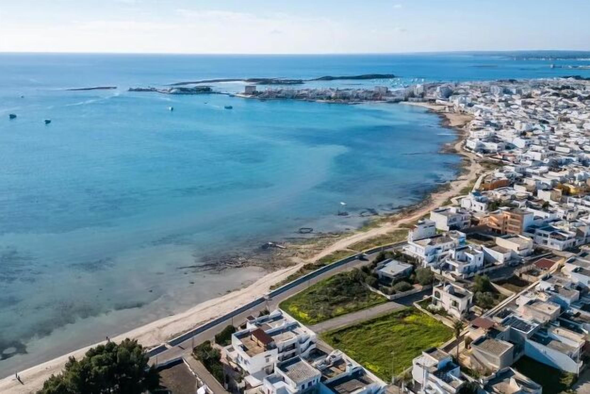 Une vue aérienne d’une ville côtière, avec des bâtiments le long du littoral, une mer bleue et limpide, et une plage de sable.