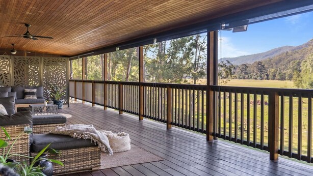 A covered outdoor deck with a wooden floor, a sofa, and a table.