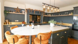 A kitchen with a central island, bar stools, a wine bottle, and a hanging light fixture. - Arbour House Farm Bungalow (Durham)