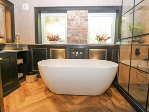 A modern bathroom with a freestanding bathtub, wooden flooring, and a brick accent wall. - Arbour House Farm Bungalow (Durham)