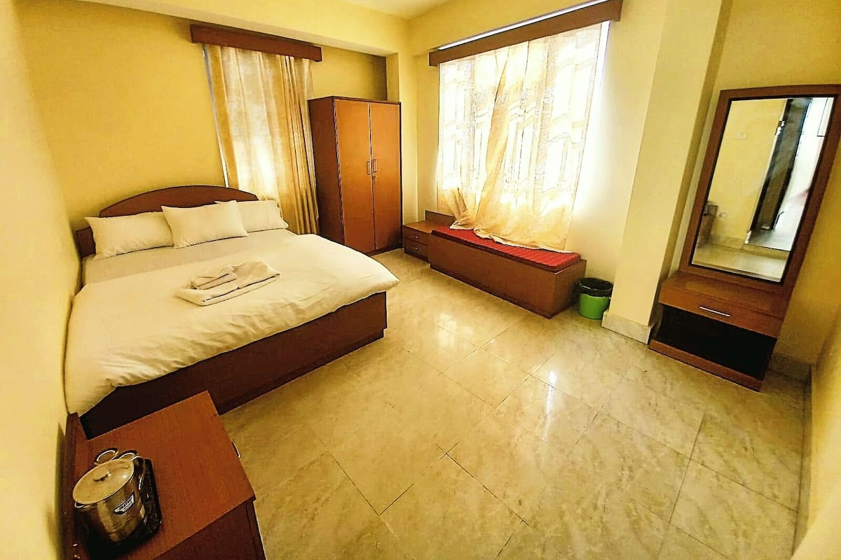 A hotel room with a bed, a wardrobe, a bench, a mirror, and a small table with a candle.