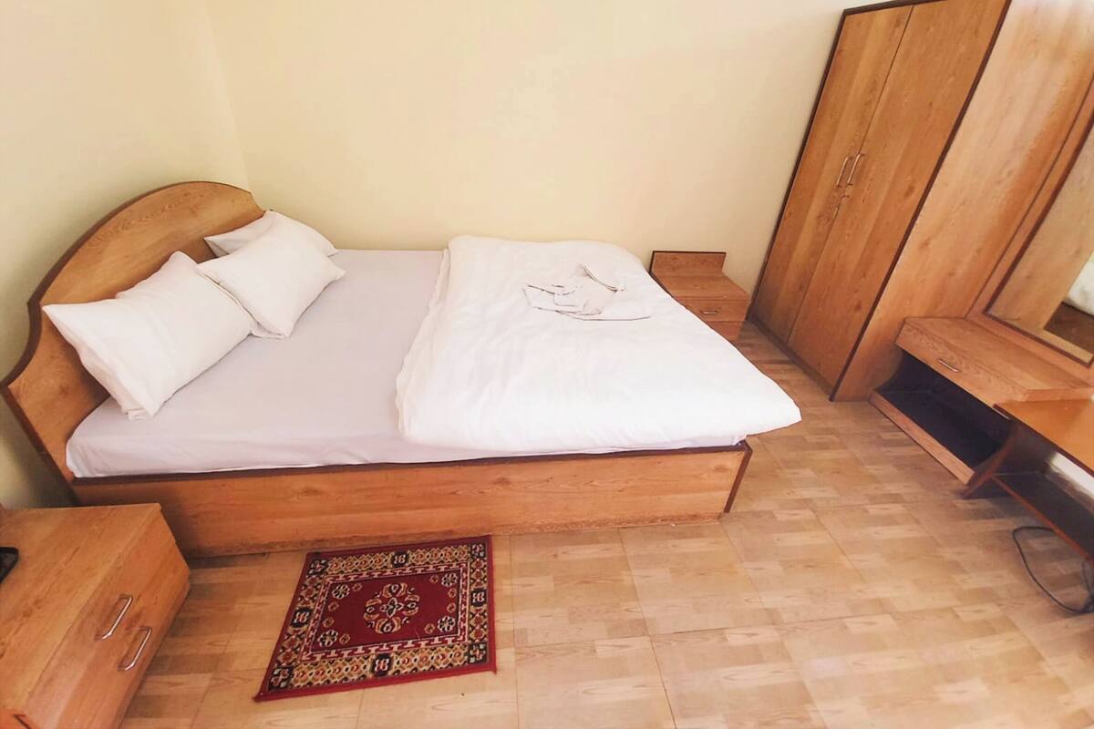 A single bed with a wooden headboard, a wooden wardrobe, and a small bedside table.