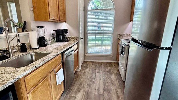 A kitchen with wooden cabinets, a stainless steel refrigerator, a built-in oven, and a window with blinds. - Covered JM Ranch - 3BR/2BA - Family Friendly (Lubbock)